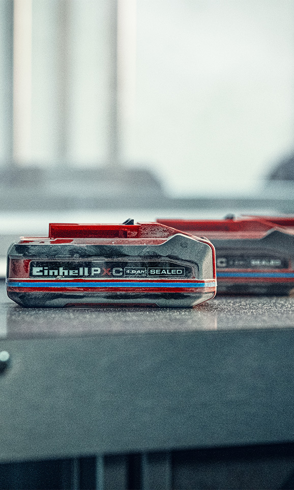 Einhell Sealed Power X-Change battery on a workbench in an industrial setting.