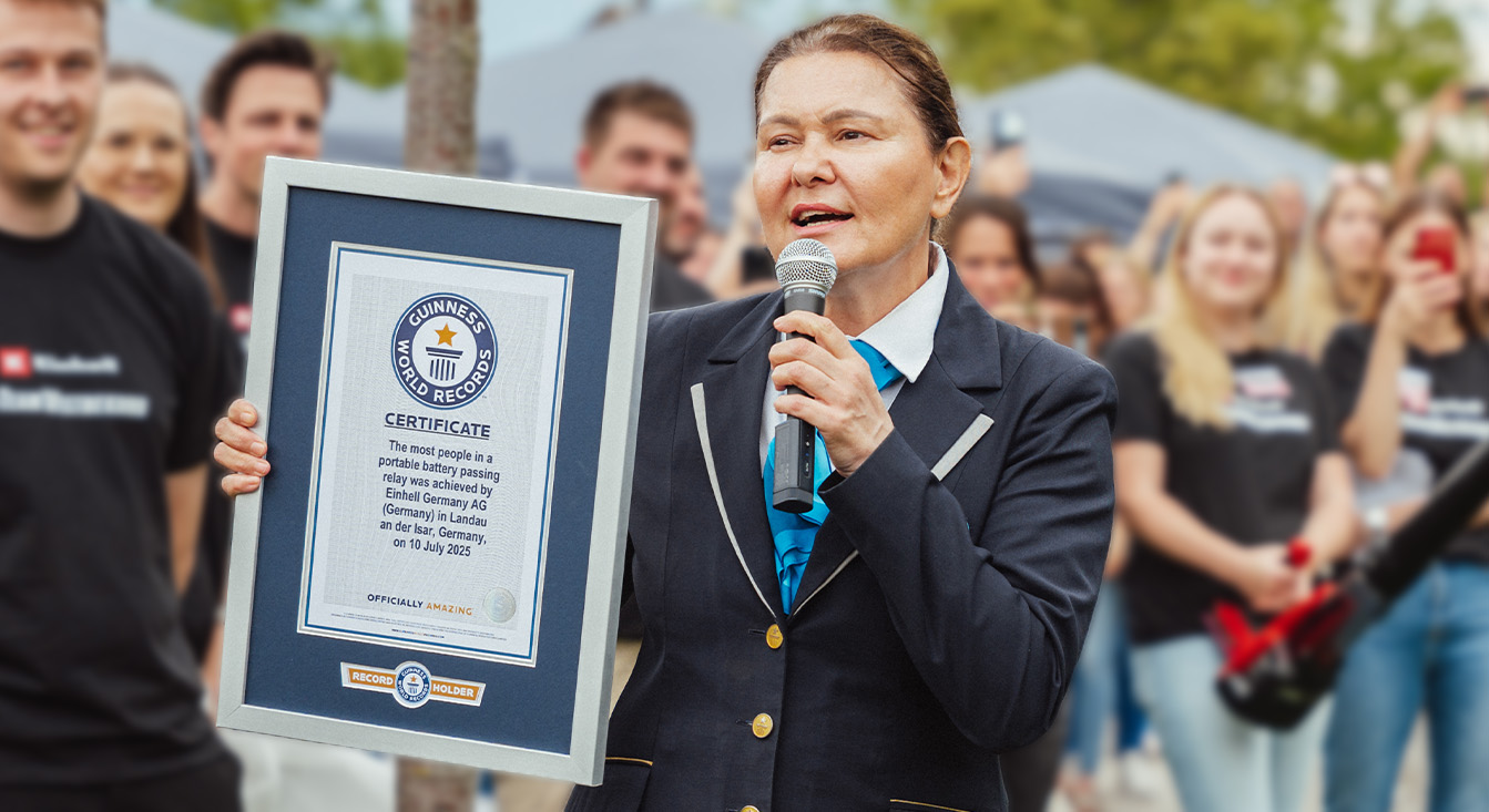 Una mujer con el uniforme oficial de Guinness sostiene un certificado del récord mundial de relevos inalámbricos de Einhell.
