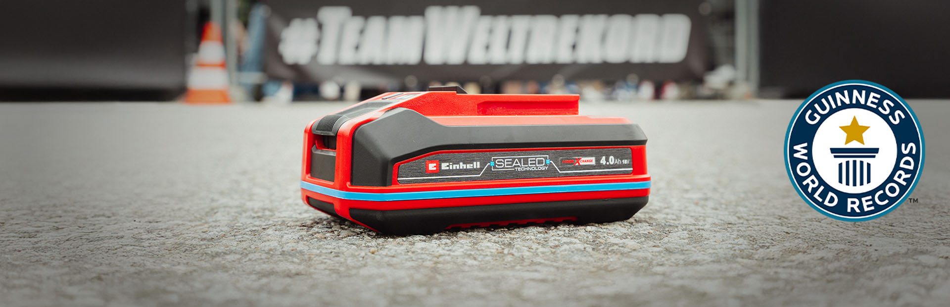 Una batería Einhell SEALED Power X-Change de 4.0 Ah yace sobre asfalto, con el logo de "Record Holder" de Guinness World Records a la derecha.