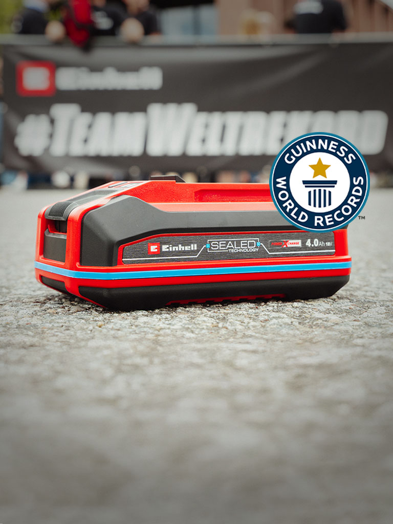 Una batería Einhell SEALED Power X-Change de 4.0 Ah yace sobre asfalto, con el logo de "Record Holder" de Guinness World Records a la derecha.