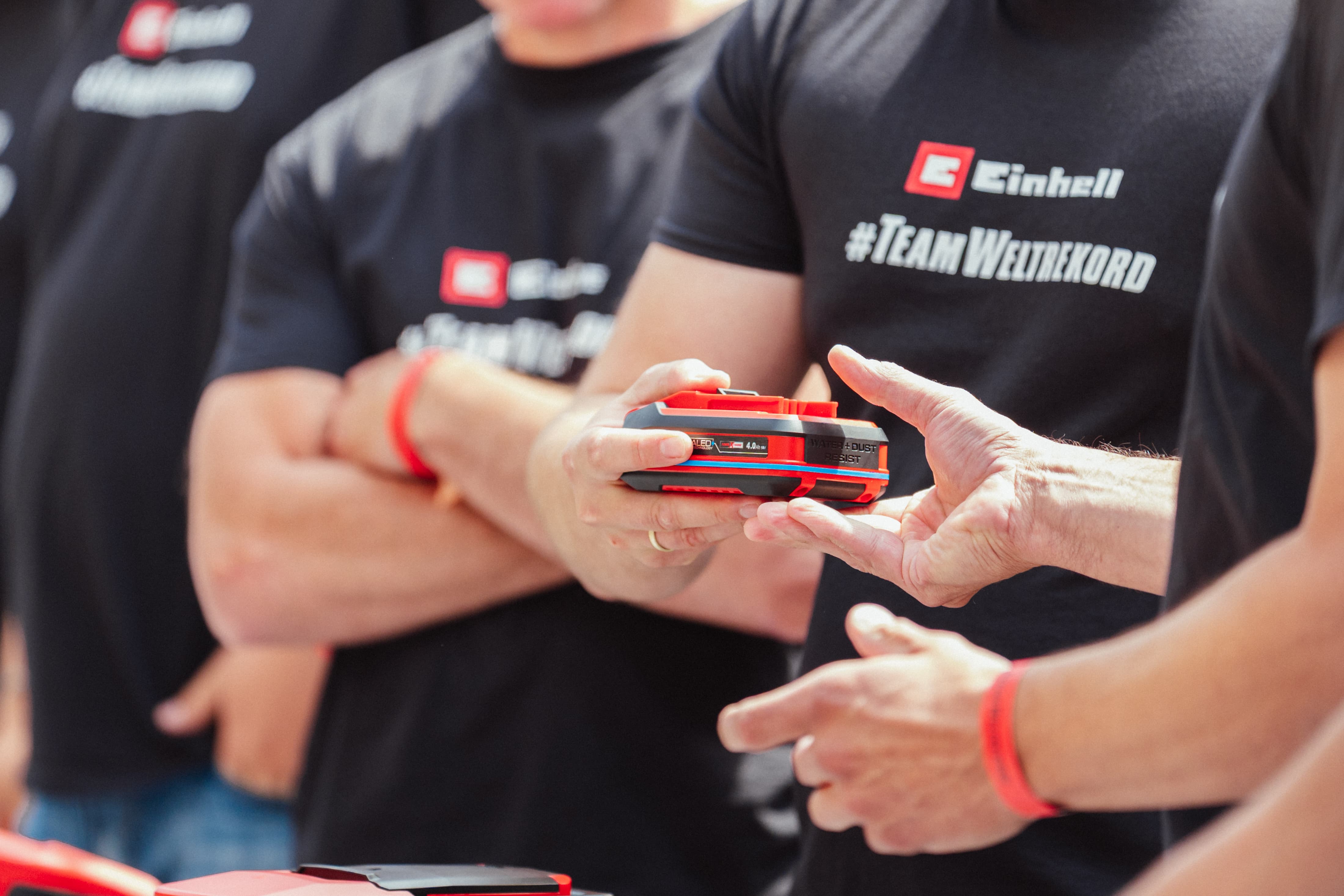 Primer plano de la entrega de una batería Einhell SEALED Power X-Change de 4.0 Ah entre dos personas.