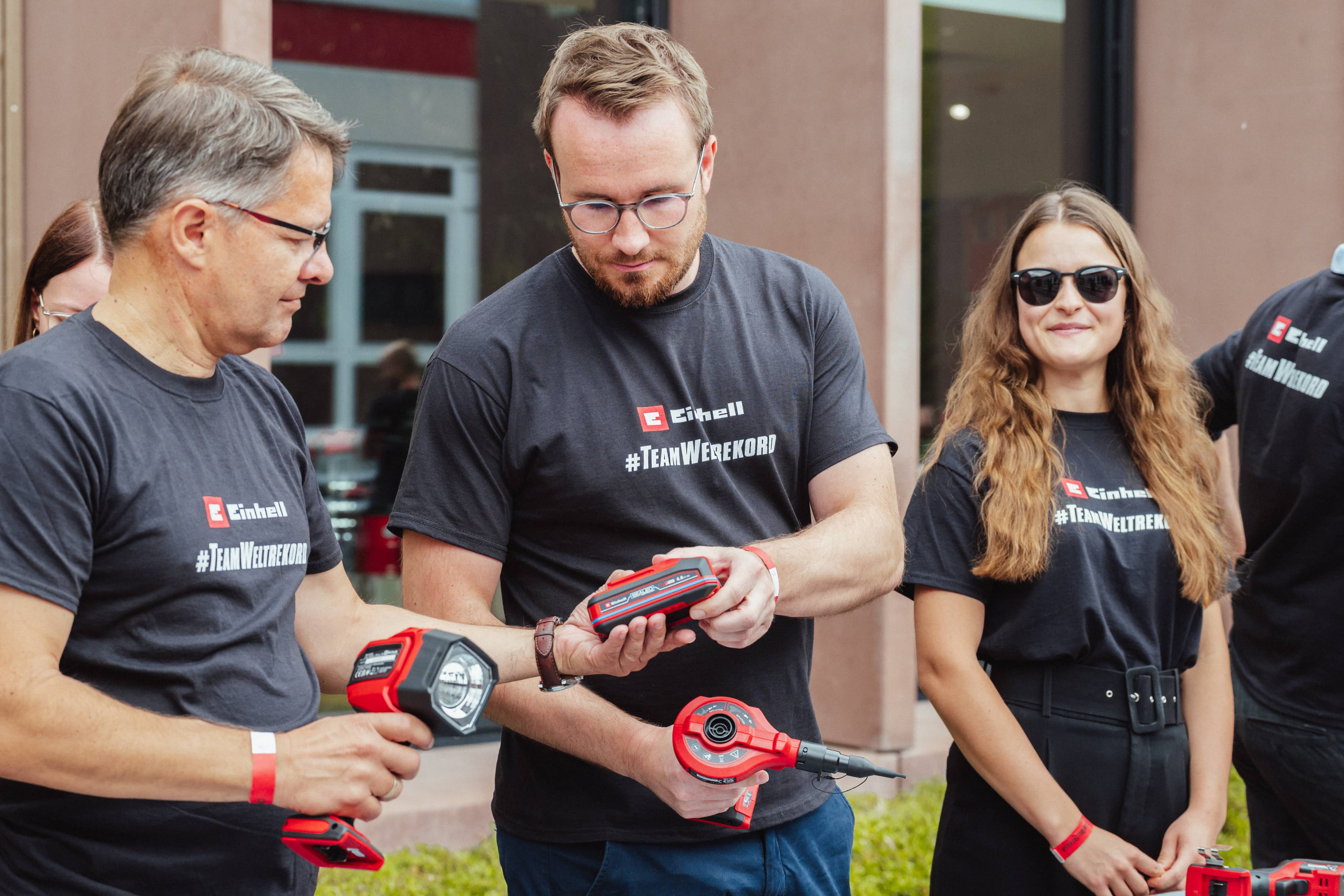 Tres personas con camisetas de "#TeamWorldRecord" examinan juntas una batería SELLADA de Einhell.